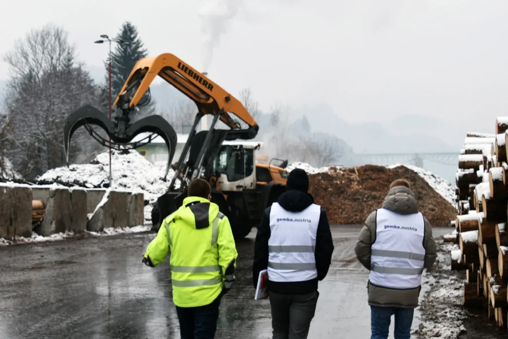 gemba.akademie Teilnehmer gehen eine Runde durch das Firmengelände auf einen Bagger zu