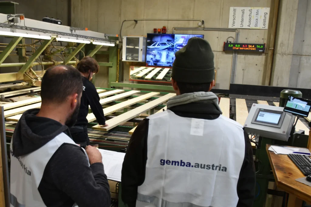 2 Teilnehmer der gemba.akademie in Sicherheitsweste stehen an Produktionsmaschine und besprechen etwas