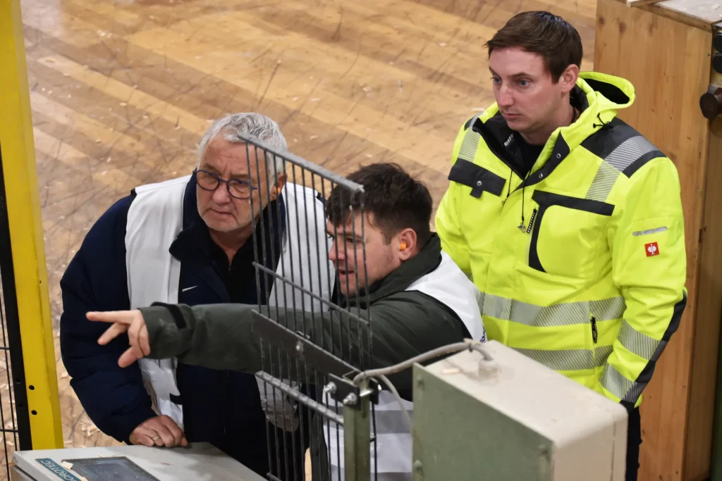 3 Teilnehmer der gemba.akademie in Sicherheitsweste besprechen etwas am Firmengelände und zeigen auf etwas